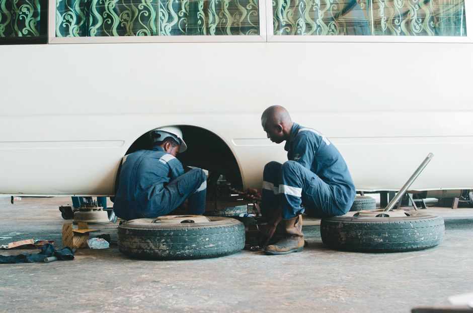 Two auto mechanics working on repairing a vehicle's wheel in a garage setting.